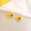 Detailed macro view of yellow sunflower stud earrings on white marble background - Yellow