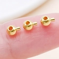 Three gold-plated copper crimp beads for jewelry making held on a fingertip - Round / 4.7x3.5mm Hole 1mm / Imitation Gold