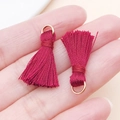 Vue à la main d'une paire de mini glands rouges de 23mm avec des anneaux dorés - Bordeaux