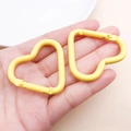 Coppia di moschettoni a cuore in lega di alluminio giallo brillante tenuti in mano - Giallo