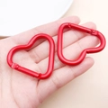 Moschettone in alluminio rosso a forma di cuore tenuto in mano per mostrarne la taglia - Rosso
