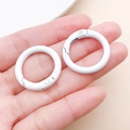 Pair of 25mm white painted zinc alloy round spring buckles held for size reference - Thick 25mm Inner Diameter 18mm / White