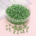 DIY green transparent 4mm glass seed beads in a clear storage box on pink background - Green