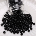Polished black glass seed beads poured from a clear bottle onto a white ceramic plate - Painted Round Beads (#10)
