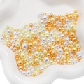 Mixed sizes of white, yellow, and orange ABS imitation pearls on a white petal tray - 3-8mm / Rhodium Plated Champagne