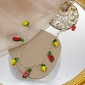Detalle de collar dorado con dijes de frutas sandía y cereza sobre un espejo - Collar de Frutas