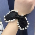 Détail d'un chouchou noeud en dentelle noire avec perles blanches porté au poignet - Noir