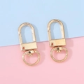 Two shiny gold U-shaped lobster clasps for DIY keychains and bags on pastel background - KC Gold