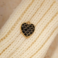 Macro shot of heart-shaped gold pendant with black enamel fish scale pattern on knit fabric - Black
