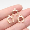 Three golden horseshoe pendants in alloy for DIY jewelry held by hand for scale - Gold