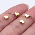 Miniature gold heart-shaped zinc alloy beads for DIY jewelry making shown on fingertips - Gold