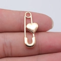 Pendentif épingle de sûreté en forme de cœur doré poli montré entre les doigts - Or KC
