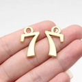 Pair of gold number 7 pendants for DIY jewelry making shown on a fingertip - Antique Gold Number 7 (D10702)