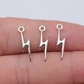 Three small silver-colored metal lightning bolt charms for DIY jewelry making on a finger - White K Gold