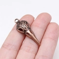 35mm antique bronze bird skull pendant shown between fingers to demonstrate scale - Antique Red Copper