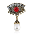 Macro shot of retro devil eye brooch with red gemstone, rhinestones and drop pearl - Red Antique Gold