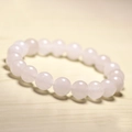 Close-up of pink quartz beaded bracelet with translucent stones on a light wood surface - 6mm / White Chalcedony
