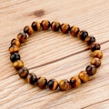 Bracciale di perle in pietra occhio di tigre giallo naturale su sfondo in legno chiaro - Stile Occhio di Tigre (1)