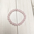 Detailed top view of 8mm pink quartz beads bracelet on a minimalist wood background - Rose Quartz