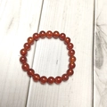 Macro shot of 8mm polished reddish-brown agate beaded bracelet on white wood - Red Agate