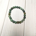 Top-down view of 8mm mottled green stone beads bracelet on white wood texture - African Pine Stone