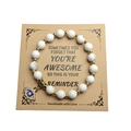 Close-up of handmade white marble beads bracelet with golden Evil Eye charm on card - Howlite
