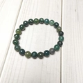 Close-up of 8mm green moss agate stone beads bracelet on a natural wood surface - Moss Agate