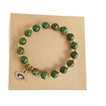 Detail of green stone beads bracelet with golden evil eye charm on a craft card - African Pine Stone
