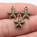 Three antique bronze starfish charms for DIY jewelry held on fingers for size comparison - Antique Bronze