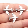 Tres colgantes de avión en plata antigua para joyas DIY sostenidos en la punta de los dedos - Plata antigua