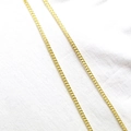 Detail einer dünnen goldenen Gliederkette auf weißem Stoff mit strukturierter Optik - Gold