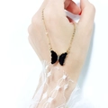 Detail of a gold-tone necklace with a black butterfly pendant held by hand with lace - Black