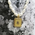 Detailed macro view of an oval pearl necklace featuring a gold letter B pendant with gems - Letter B