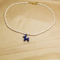 Detail of a blue balloon dog pendant on a white pearl necklace with golden metal clasp - Blue