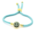 Macro detail of hand-woven light blue cord bracelet with a gold-plated smiley face charm - Light Blue Braided Smiley (A5)