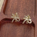 Close-up of gold-plated bow earrings with micro-pave white zircon on a wooden tray - 18K Gold Pair (Tight Bow)