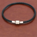 Close-up of black braided leather bracelet with matte gold magnetic clasp on brown leather - Black