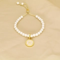Detailed macro of a pearl bracelet featuring a pink enamel initial A pendant with gold trim - Letter A
