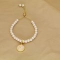 Detail of adjustable pearl bracelet with golden letter M pendant on beige fabric - Letter M