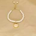 Detail of adjustable pearl bracelet with golden letter V charm on soft fabric - Letter V