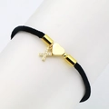 Detail of black woven rope bracelet with gold heart and zircon cross charms on a display - Letter X