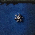 Macro shot of a silver snowflake pendant with a central zircon on blue textured fabric - Snowflake (Accessory Only)