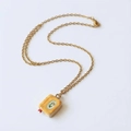 Dettaglio di una collana vintage dorata con ciondolo a forma di libro crema e decoro a foglie - Stile Libro Giallo Fiore