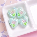 Macro shot of mint green heart-shaped resin beads with tulip patterns and iridescent finish - Qingchuan Green