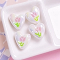 Macro detail of heart-shaped UV coated beads with tulip flower patterns for DIY jewelry - White