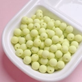 Macro detail of 6/8mm matte rubber-finish light yellow round beads in a divider tray - Fluorescent Green