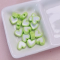 Detail van hartvormige DIY-kralen met groene randen en een wit midden in een schaal - Grootte ca. 12mm, gat ca. 2,5mm / Groen