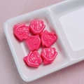 Macro detail of six pink cartoon pig acrylic beads on a white ceramic tray for DIY crafts - Rose Red