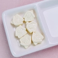 Macro detail of six cream house-shaped acrylic beads for DIY jewelry and phone charms - Off-white