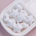 Macro view of macaron white star beads and round acrylic charms in a ceramic tray - White
